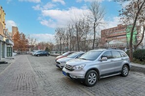 A parking area with several cars parked on a cobblestone surface, surrounded by buildings and leafless trees. - Nanshu Thatched Cottage Hotel (Huihua College Branch of Shijiazhuang Railway Station) (Shijiazhuang)
