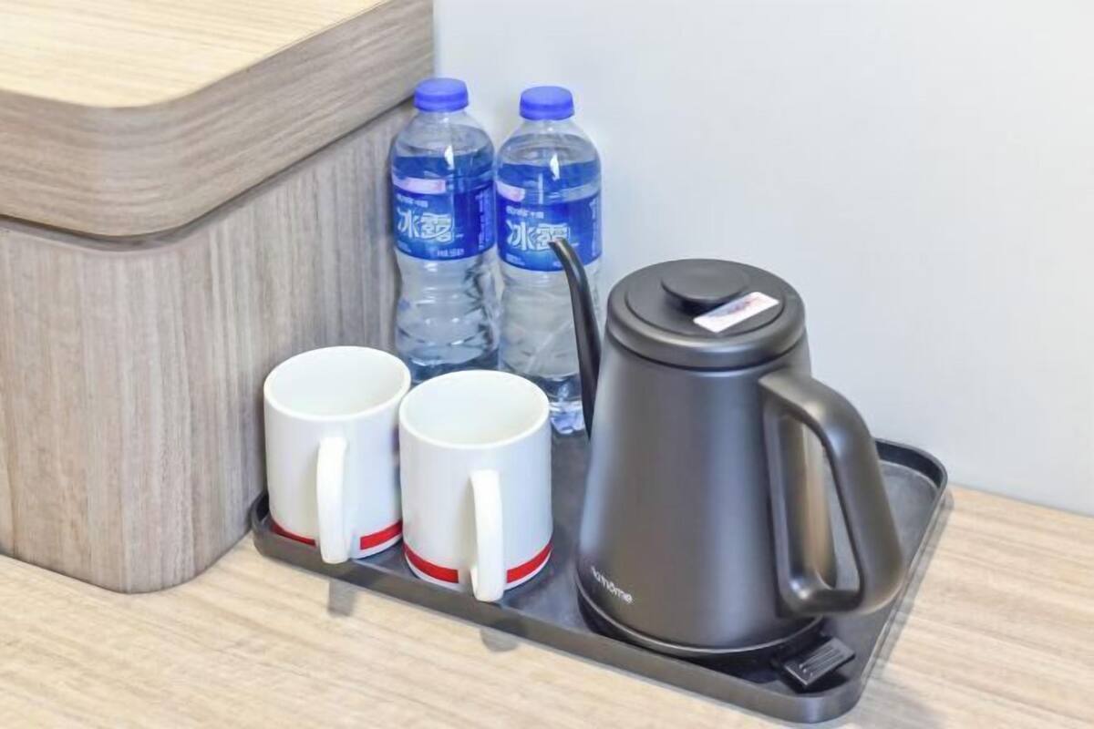 Una bandeja con dos tazas blancas, dos botellas de agua y una tetera eléctrica negra.