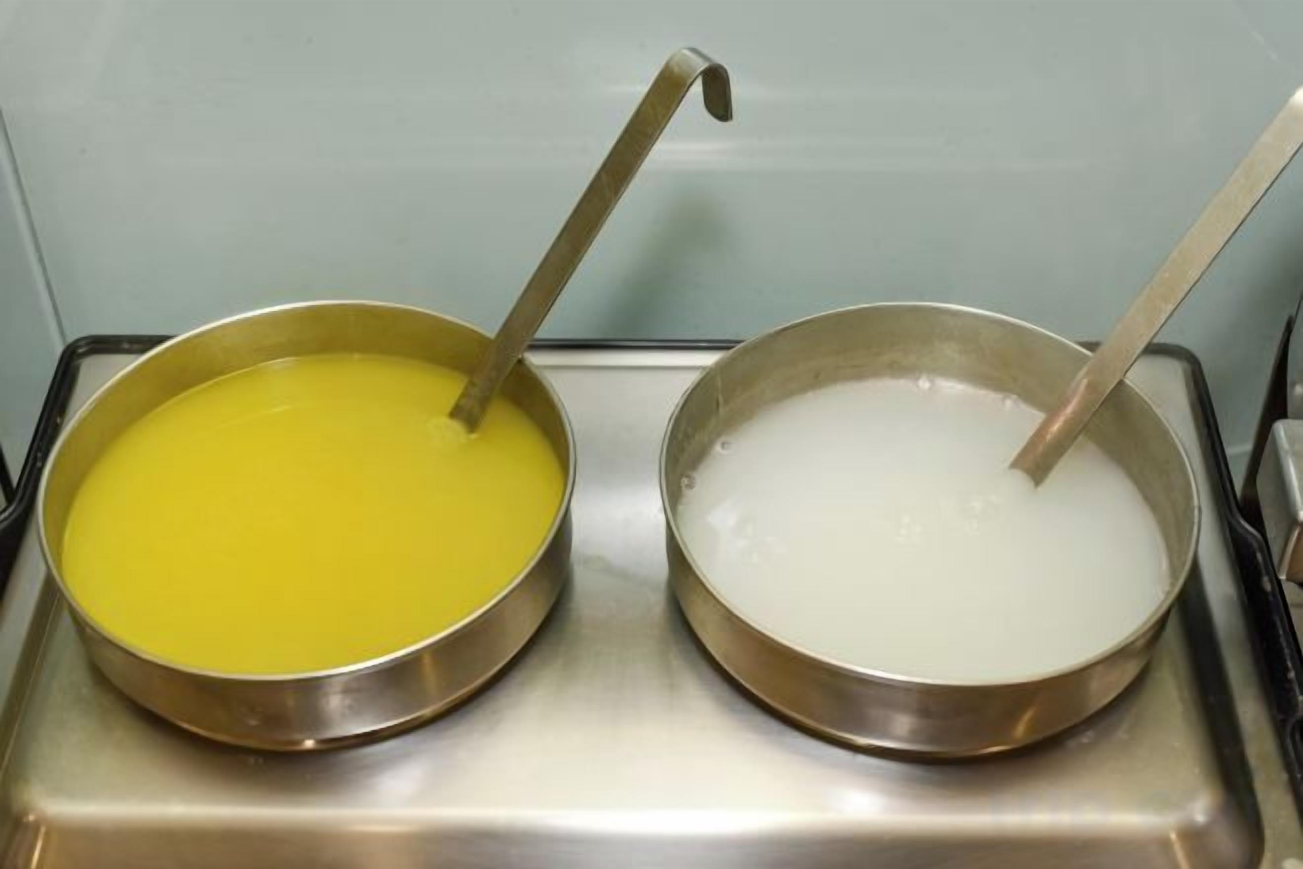 Två metallskålar står på en yta av rostfritt stål, den ena innehåller en gul vätska och den andra en vit vätska.
