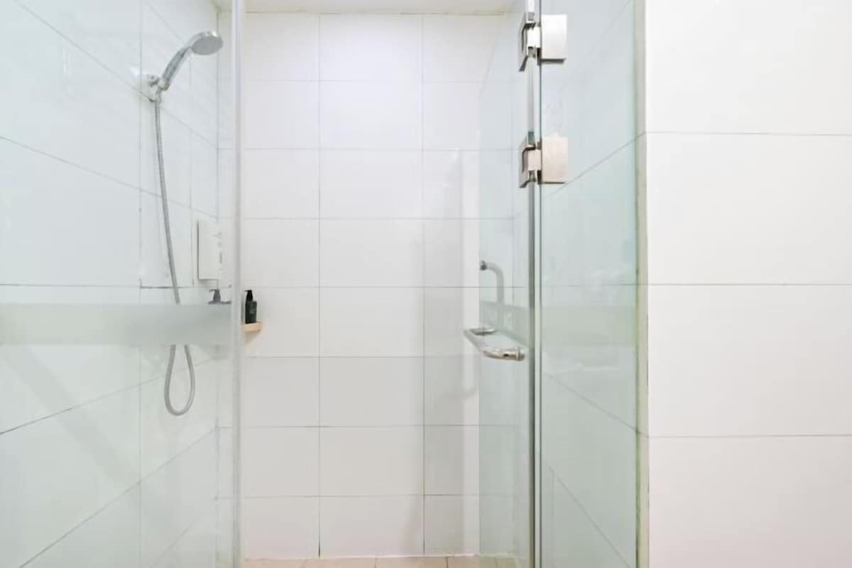 A glass-enclosed shower with a handheld showerhead and a wall-mounted faucet.