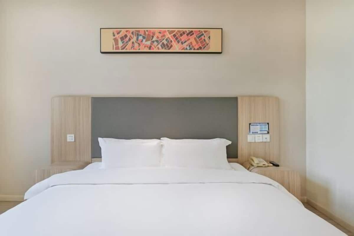 Una habitación de hotel con una cama, cabecera, teléfono de pared y un cuadro enmarcado.