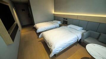 A hotel room with two beds, a sofa, a small table, and a TV.