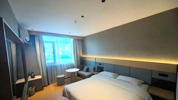 Habitación de hotel moderna con una cama grande, mesitas de noche, una pequeña mesa redonda y vistas al exterior.