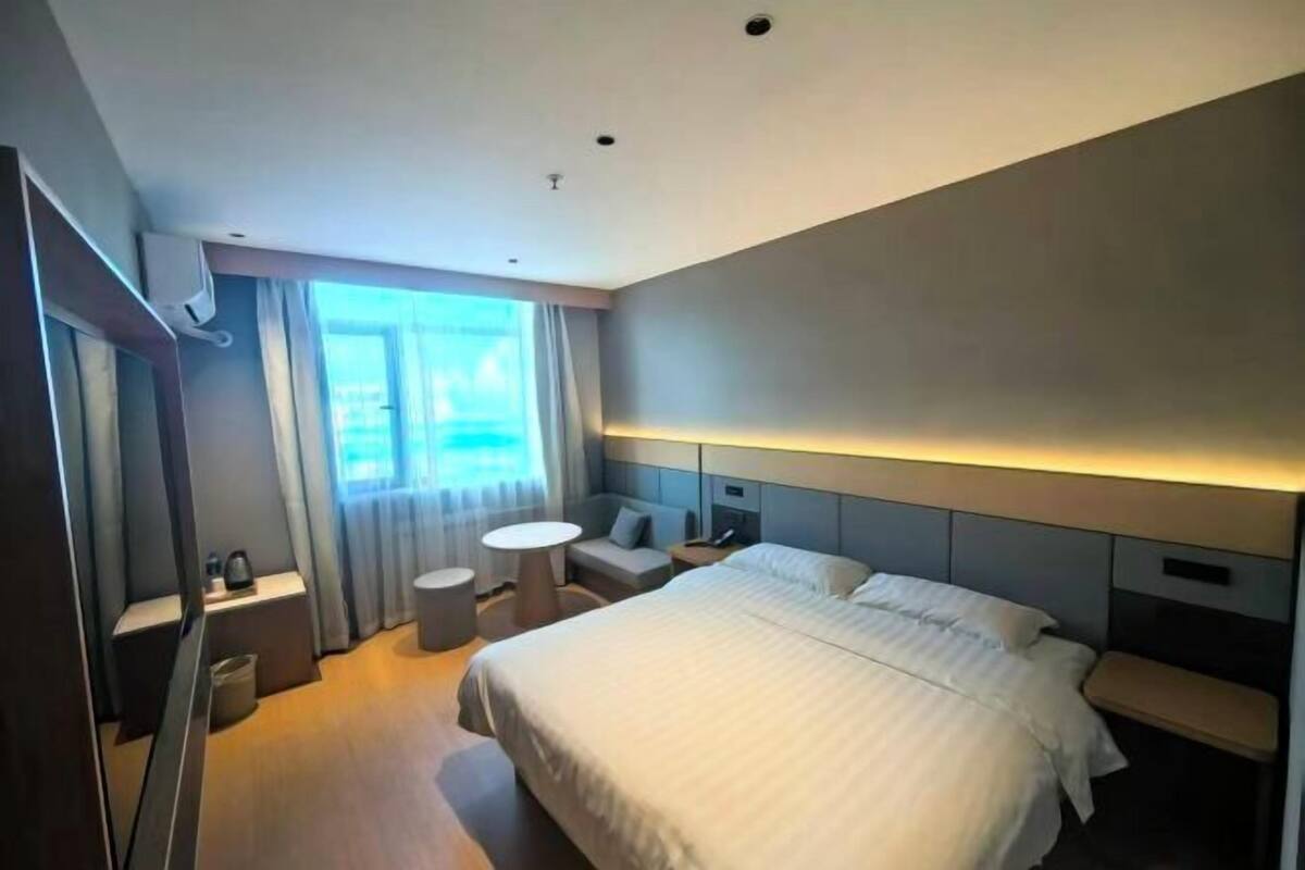 Habitación de hotel moderna con una cama grande, mesitas de noche, una pequeña mesa redonda y vistas al exterior.