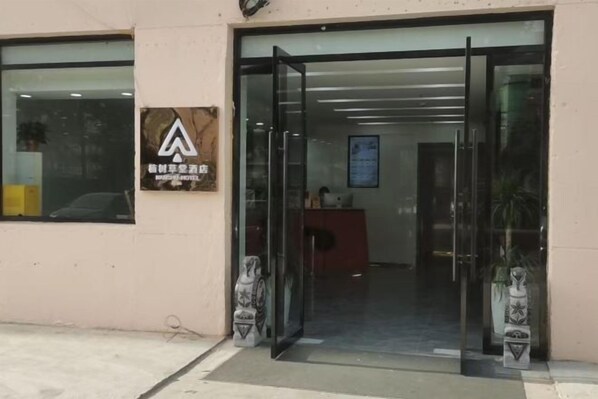Entrada de hotel con puerta de vidrio, un mostrador de recepción en el interior y un cartel en la pared.