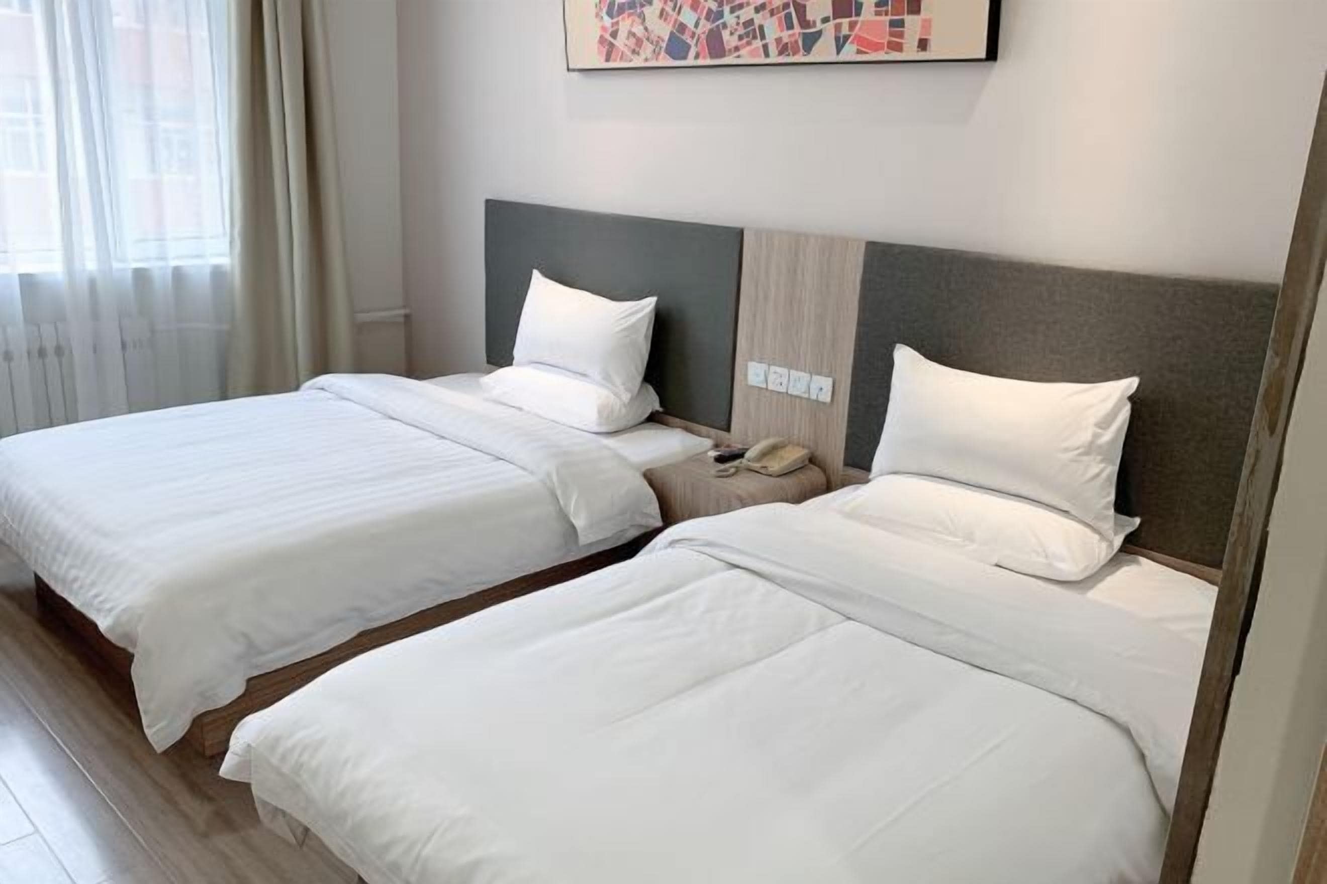 A hotel room with two beds, a nightstand, a telephone, and a window with curtains.