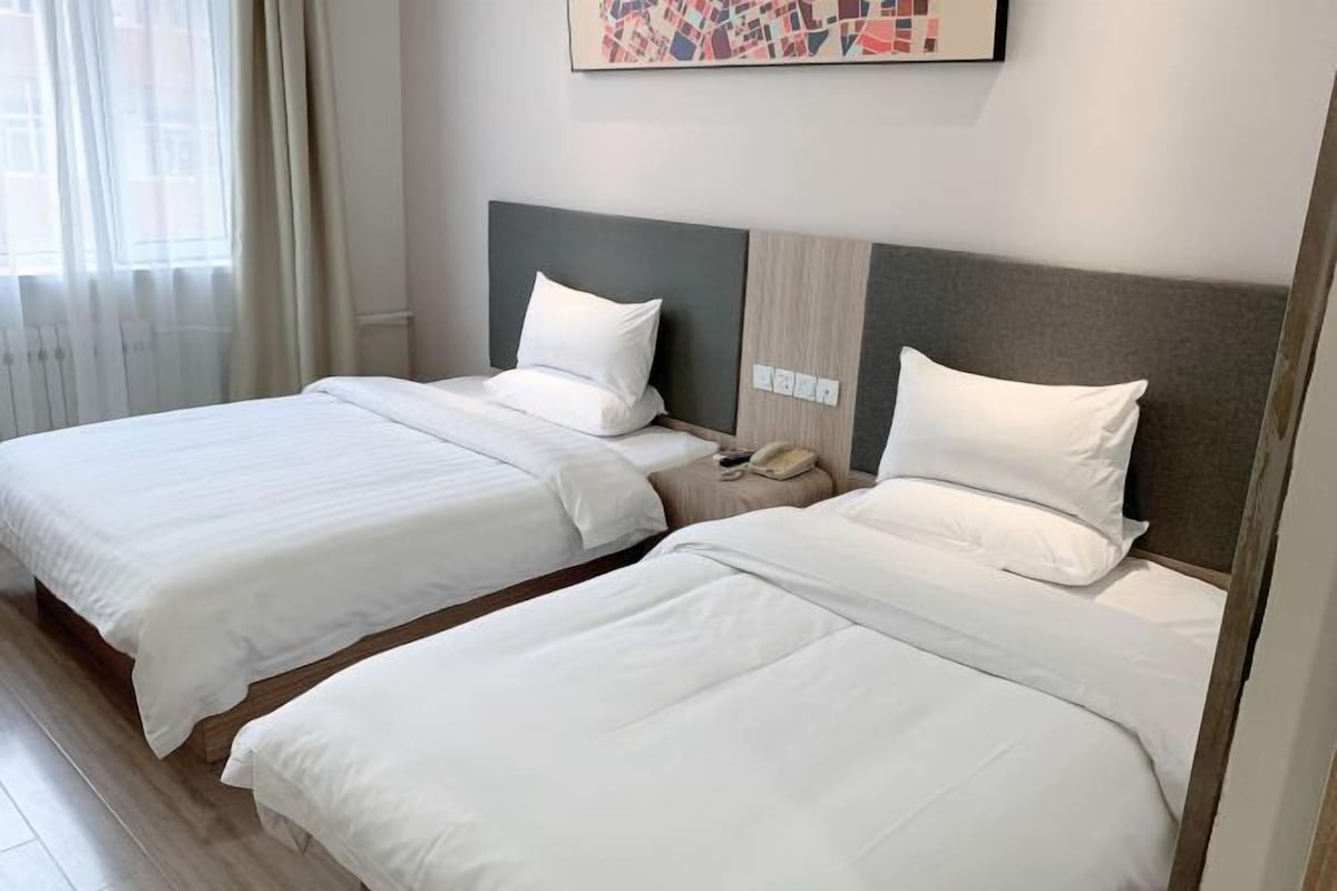 A hotel room with two beds, a nightstand, a telephone, and a window with curtains.