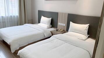 A hotel room with two beds, a nightstand, a telephone, and a window with curtains.
