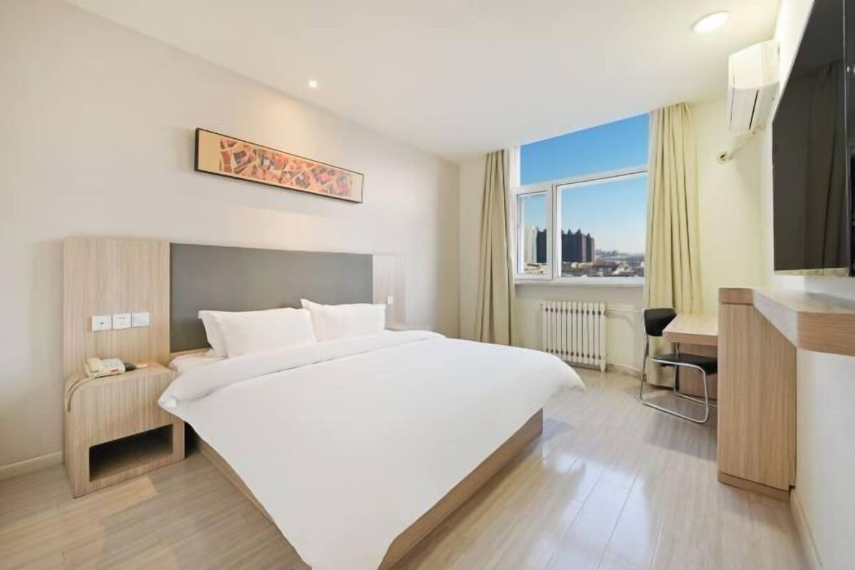 Habitación de hotel con cama, mesita de noche, escritorio, silla y vistas a la ciudad por la ventana.
