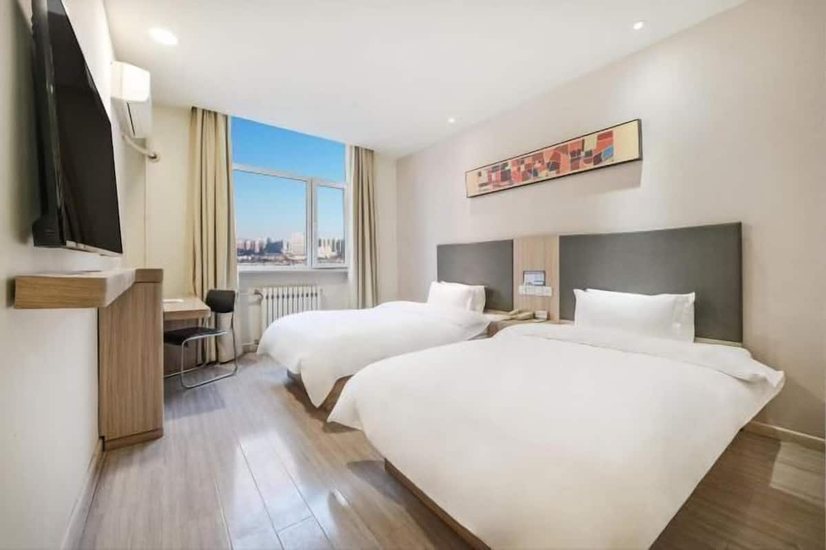 Habitación de hotel con dos camas, un escritorio, una silla, un televisor y una ventana con vistas a la ciudad.