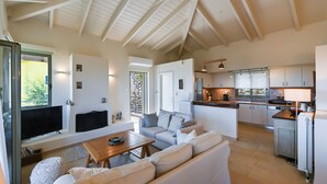 Ein modernes Wohnzimmer mit einer Couch, einem Couchtisch und einem Fernseher. Es gibt eine Küchenzeile mit Kühlschrank, Herd und Spüle.