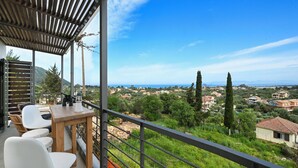 Un balcon avec une table et des chaises, donnant sur un paysage pittoresque avec des maisons et des arbres.