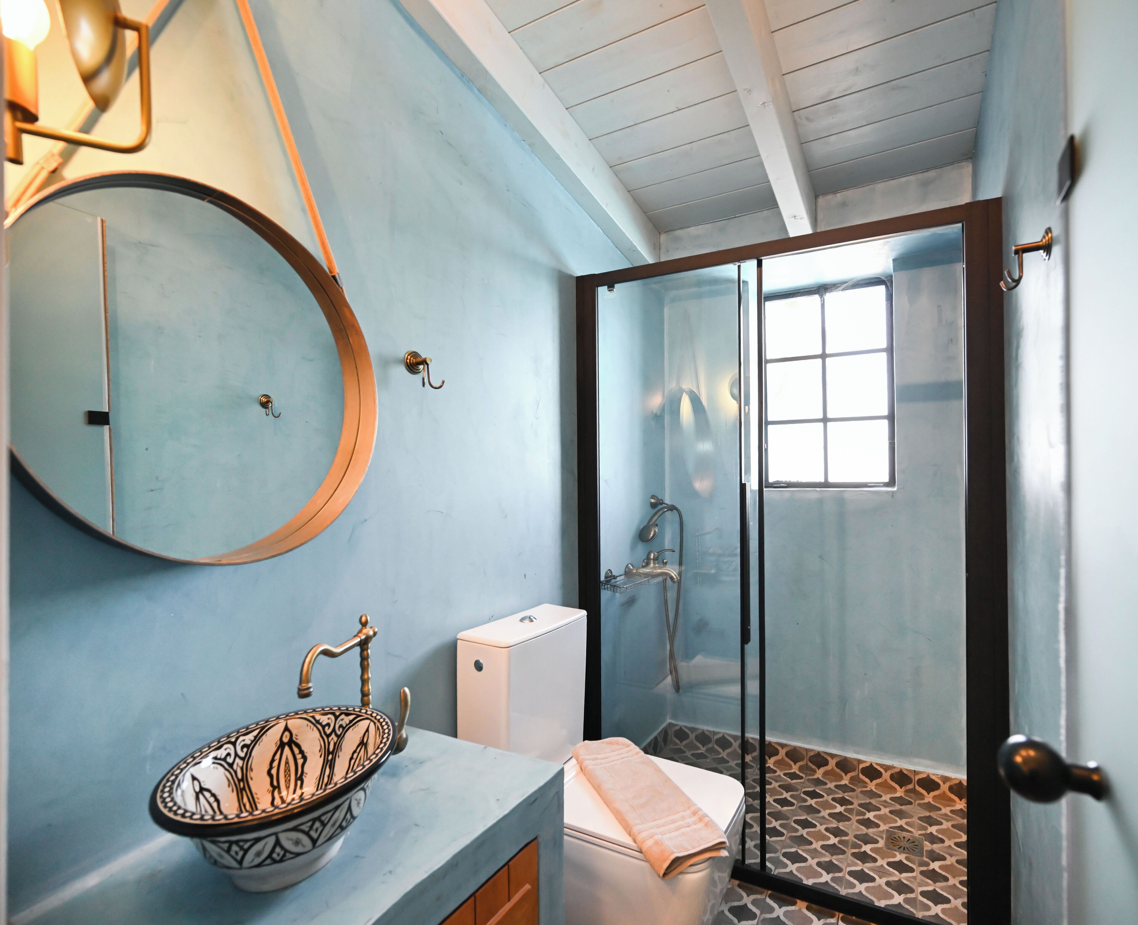 A bathroom with a round mirror, a sink with a decorative bowl, a toilet, and a shower area with a glass door.