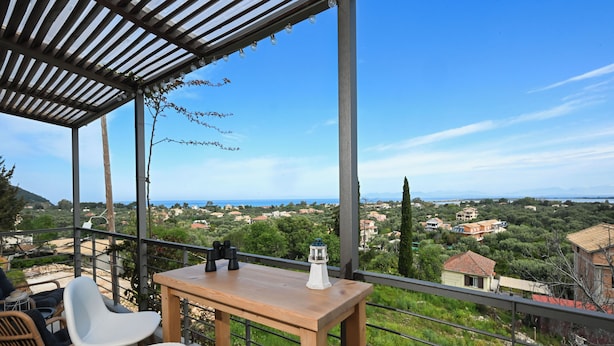 Un balcon avec une table et des chaises en bois, un télescope et une vue sur un paysage côtier.