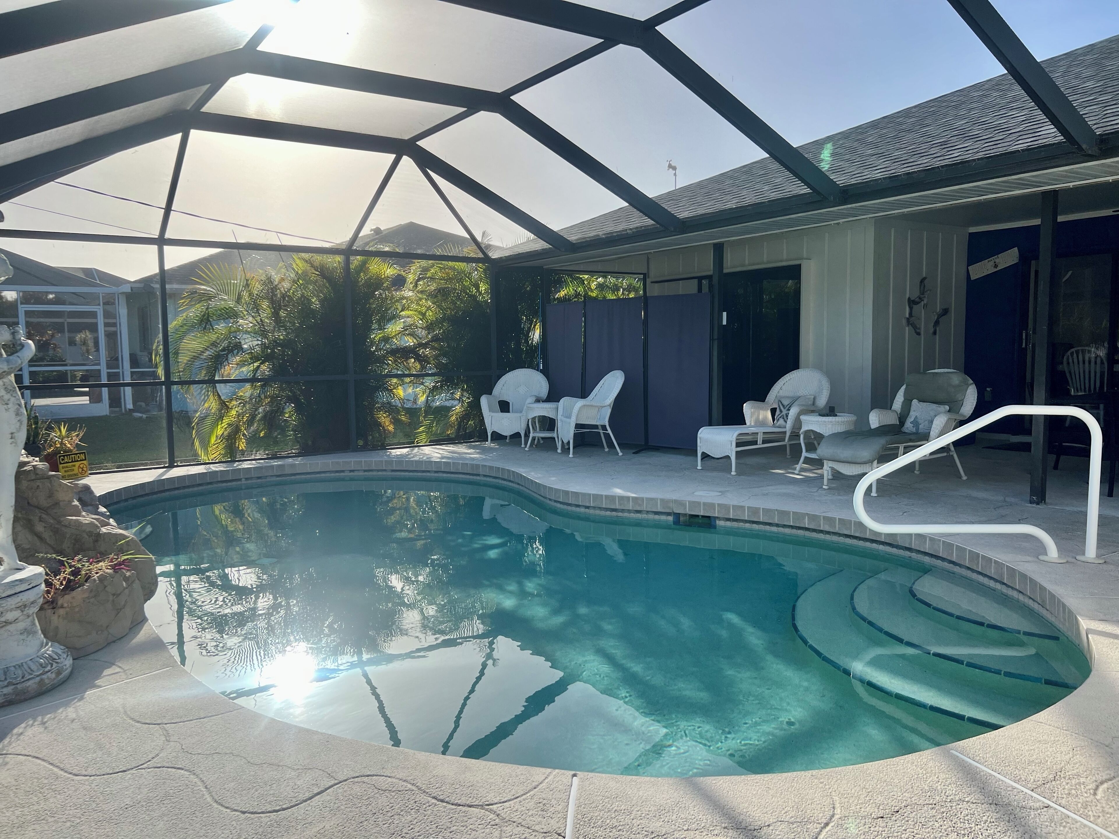 A swimming pool with a glass enclosure, surrounded by white lounge chairs and a covered patio area.