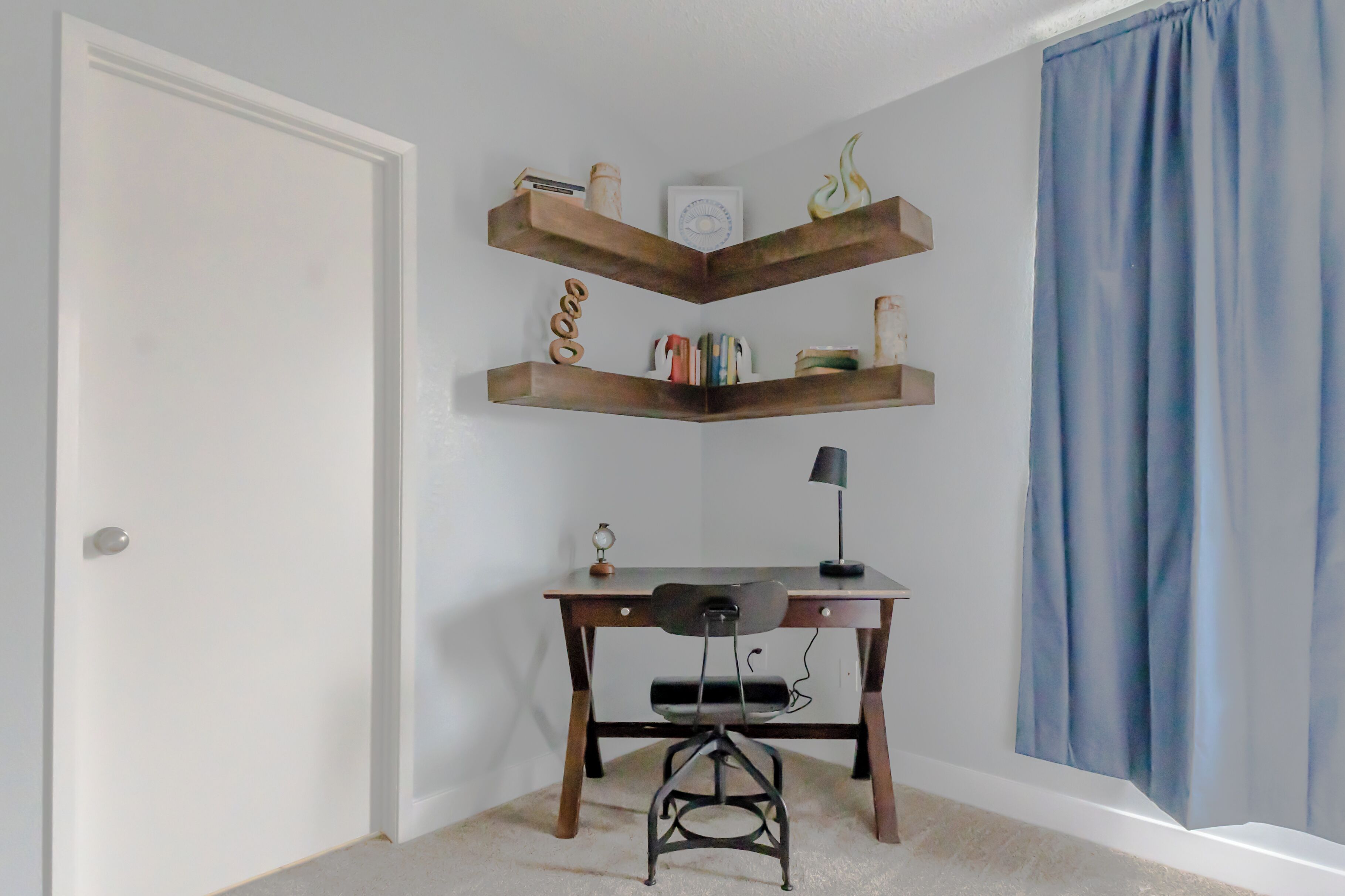 Habitación de esquina con escritorio, silla y tres estanterías de madera con diversos objetos.