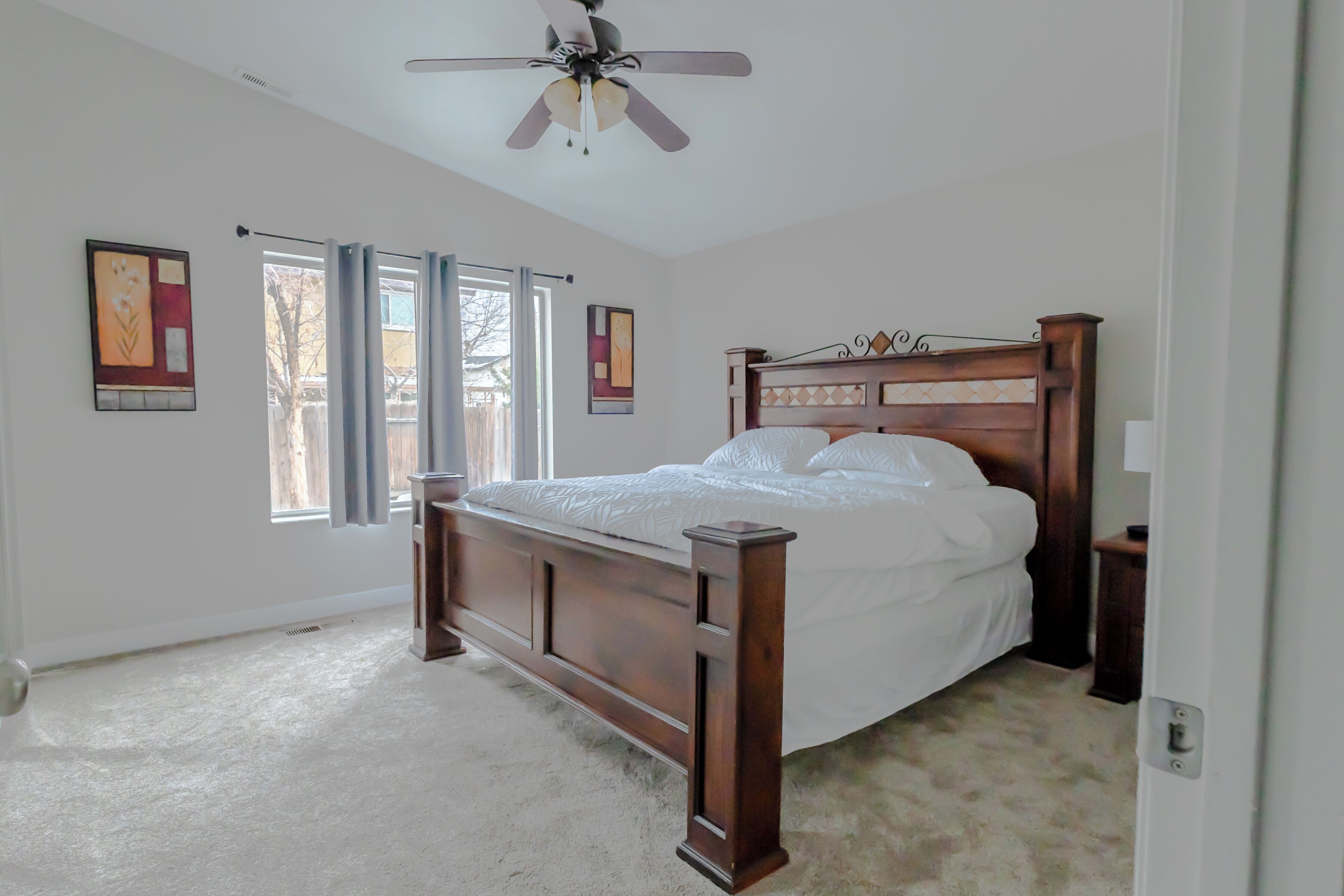 A bedroom with a wooden bed, a ceiling fan, and large windows.