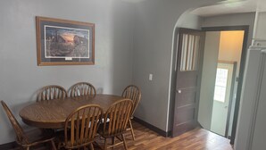 Un comedor con una mesa y sillas de madera, un cuadro enmarcado en la pared, y una puerta que da a otra habitación.