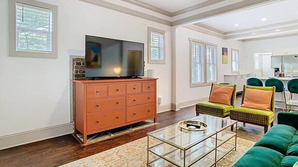Una sala de estar con un televisor sobre un mueble de madera, una mesa de centro de vidrio y sillones tapizados de color verde.
