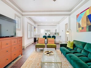A living room with a television, a sofa, two armchairs, a coffee table, and a dining area in the background.