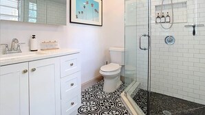 Un baño con inodoro blanco, cabina de ducha con mampara de vidrio y suelo estampado.