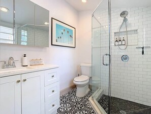 Un bagno con un water bianco, una cabina doccia in vetro e un pavimento a motivi.