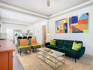 A modern living room with a sofa, chairs, and a coffee table. There is a kitchen in the background. - Bungalow on Shine (Orlando)