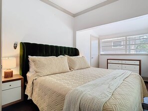 A bedroom with a bed, a nightstand, a dresser, and a window with blinds.