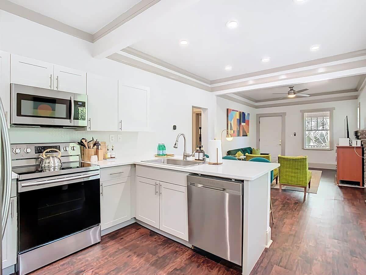 A modern kitchen with white cabinetry, stainless steel appliances, and a wooden floor.