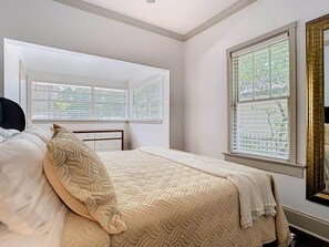 A bedroom with a bed, a window with blinds, and a mirror with a gold frame.