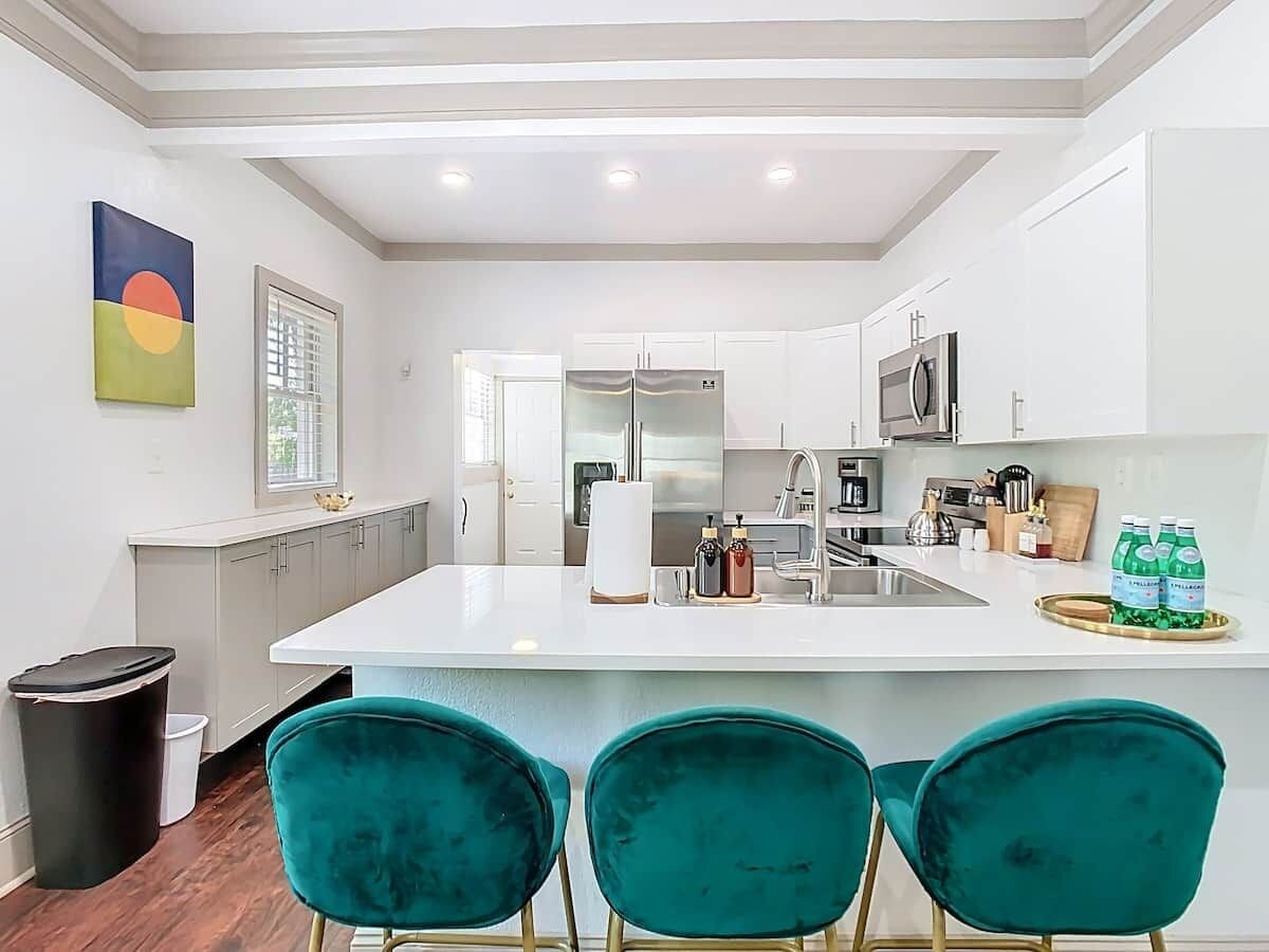 A modern kitchen with white cabinets, a central island, and teal chairs.