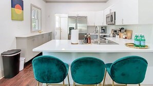 Una cocina moderna con armarios blancos, una isla central y sillas color turquesa.