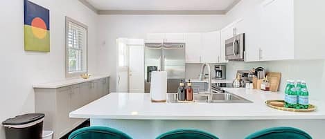 A modern kitchen with white cabinets, a central island, and teal chairs.