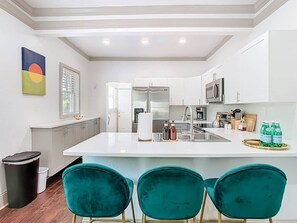 Una cucina moderna con mobili bianchi, un'isola centrale e sedie color petrolio.