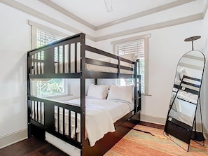 A bunk bed with a white mattress and pillows, a wooden floor, and a window with blinds. - Bungalow on Shine (Orlando)