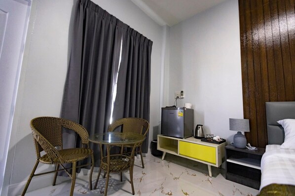 A hotel room with a bed, a nightstand, a TV, a small table with two wicker chairs, and a window with curtains. - Green Zone Resorts hotel (Sai Mun)