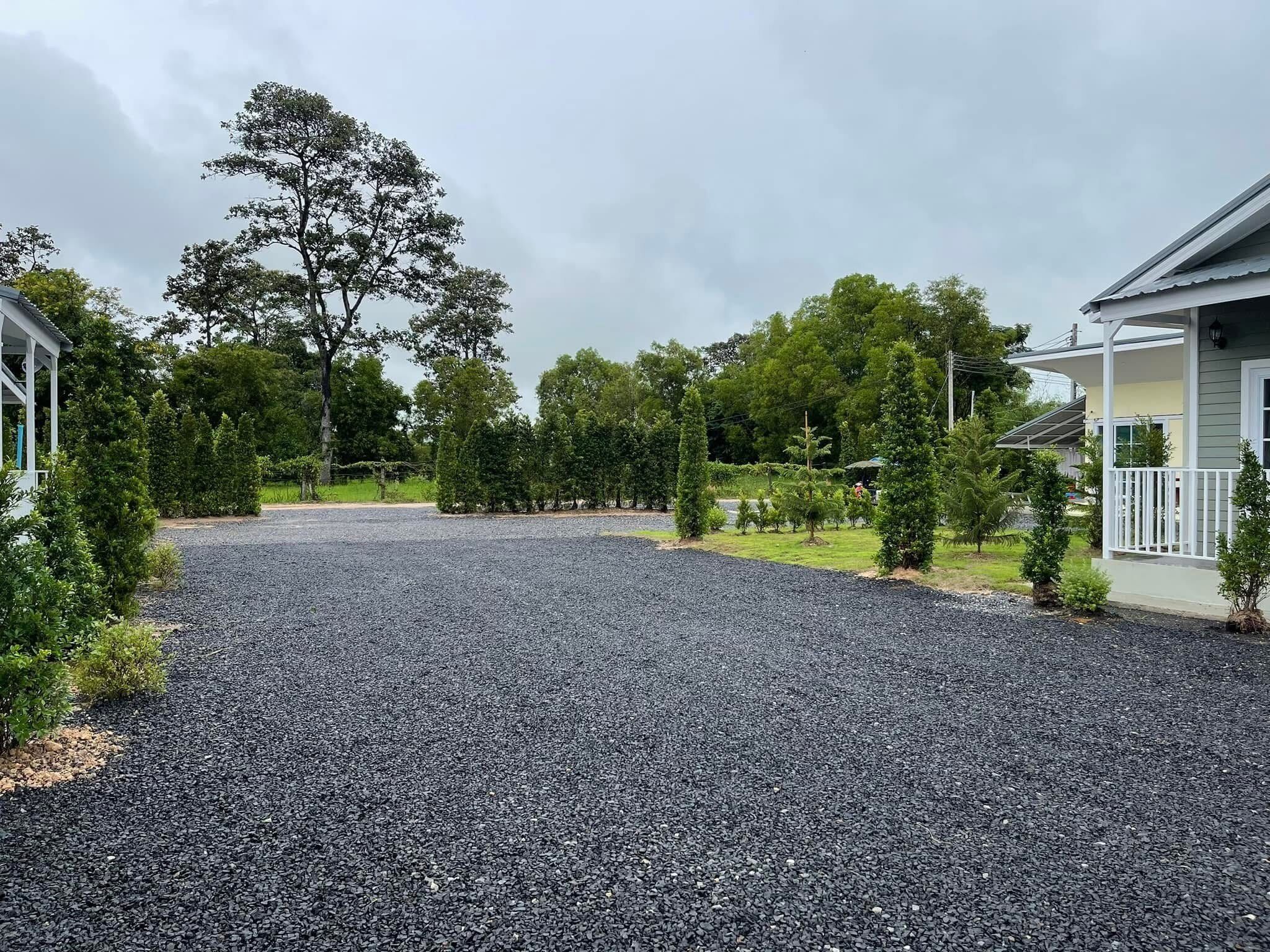 A gravel driveway leading to a residential area with houses and trees.
