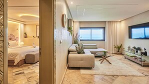 A modern hotel room with a bed, a sofa, a glass coffee table, and a TV mounted on the wall.