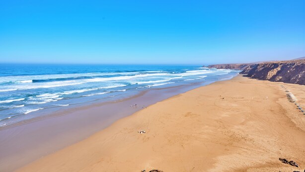 A beach with a clear sky, sandy shore, and a rocky cliff.
