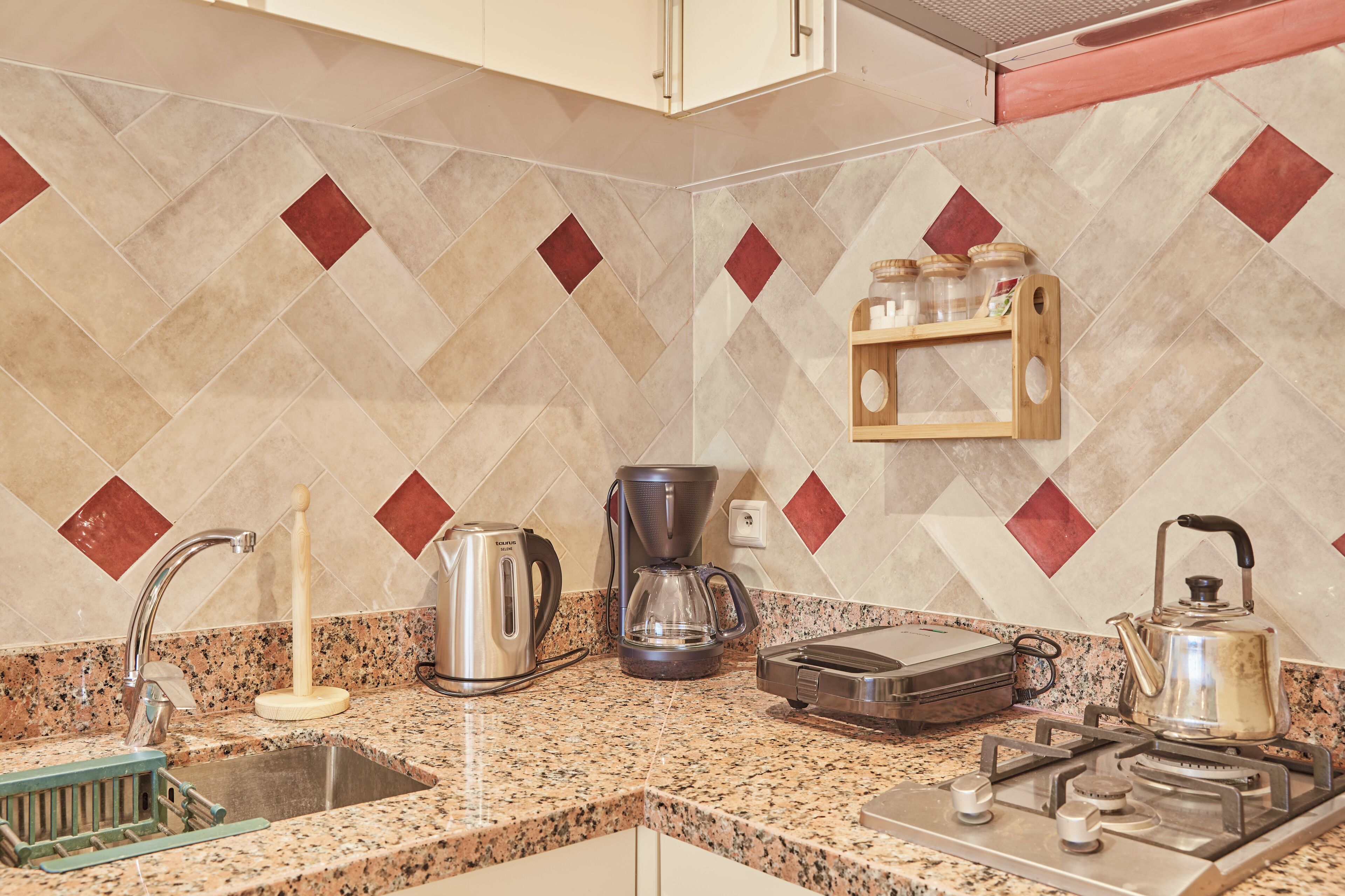 A kitchen with a granite countertop, stainless steel appliances, and a herringbone-patterned backsplash.