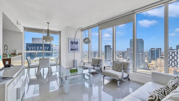 A modern living room with a glass coffee table, white sofas, and a city view.