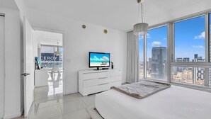 A modern hotel room with a large bed, a TV, a city view, and a white interior.