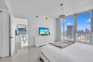 A modern hotel room with a large bed, a TV, a city view, and a white interior.