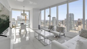 A modern living room with a large window, a flat-screen TV, a glass coffee table, and a sofa with patterned cushions.