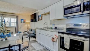 A modern kitchen with white cabinets, a stainless steel stove, and a microwave. There is a dining table with chairs and a vase with flowers.