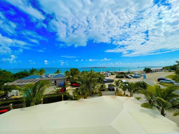 A beachside parking area with cars, a small building, and palm trees. - Beautiful apartment with sea view (Marigot)