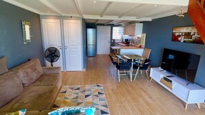 A spacious living area with a wooden staircase, a sofa, a TV, and a dining area. - Beautiful apartment with sea view (Marigot)