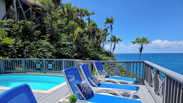 A poolside area with blue lounge chairs and a small table with a plant, overlooking a clear blue ocean. - Ocean Front 4 Bedroom with Private Pool (St. Thomas)