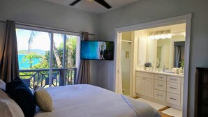 A bedroom with a bed, a ceiling fan, a TV, and a view of the ocean. - Ocean Front 4 Bedroom with Private Pool (St. Thomas)