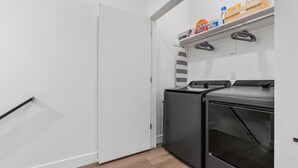 A laundry room with a dryer, washing machine, and shelves with laundry supplies. - Summer Getaway: Hot tub & Cold Plunge, Gear-dryer (Salt Lake City)